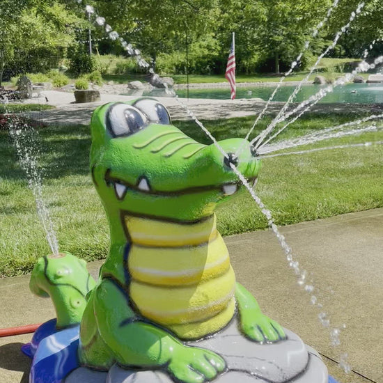 Alligator splash pad water play feature with bright green body and yellow belly, spraying water streams for kids’ outdoor fun.