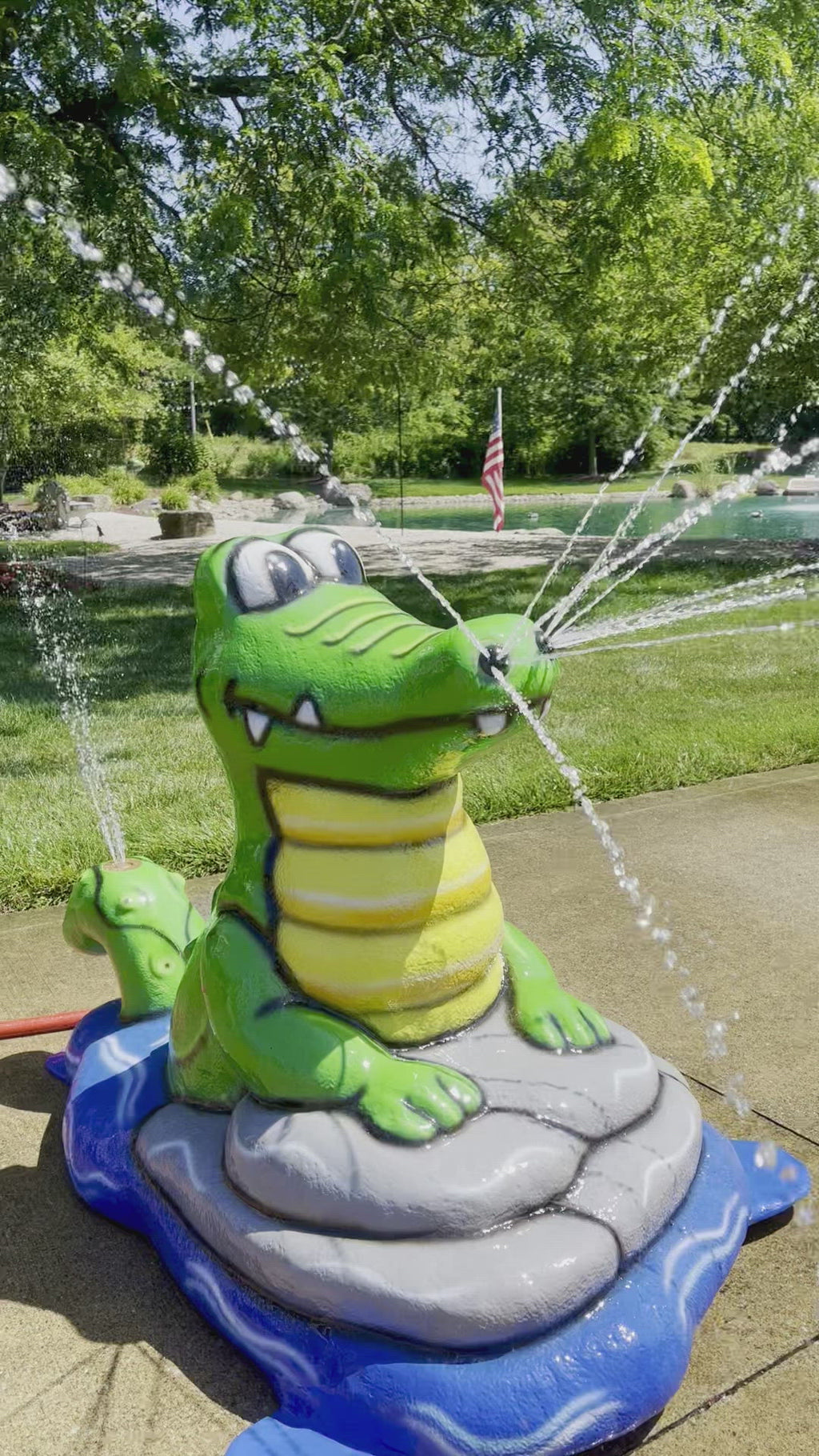 Alligator splash pad water play feature with bright green body and yellow belly, spraying water streams for kids’ outdoor fun.