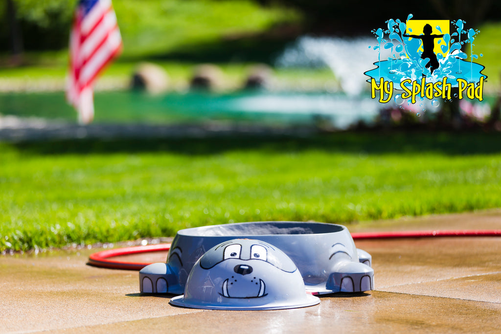 Dog Park Bulldog Water Bowl Water Play Feature by My Portable Splash Pad – gray bulldog-shaped water bowl on outdoor concrete with grass and American flag in background.