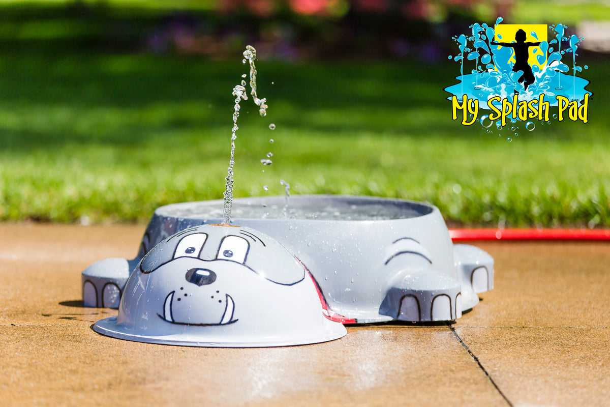Dog Park Bulldog Water Bowl Water Play Feature by My Portable Splash Pad – gray bulldog-shaped water bowl spraying water on outdoor concrete surface with grass in background.