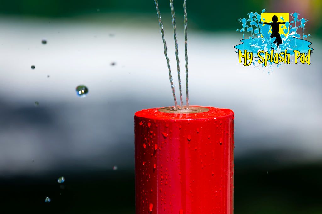Close-up of tall red Rain Stick Splash Pad Water Play Feature nozzle spraying water streams upward.