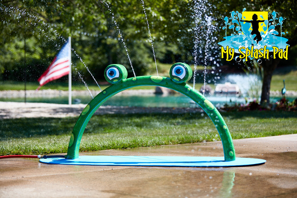 Mini Frog Arch Mobile Water Play Feature by My Portable Splash Pad – green arch with frog eyes spraying water streams on outdoor concrete with grass and American flag in background.